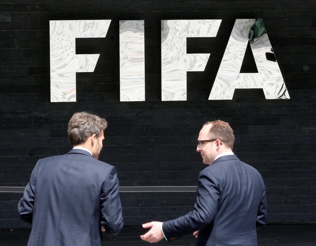 Two men talk to each other in front of the FIFA logo at the FIFA headquarters in Zurich, Switzerland, Wednesday, May 27, 2015. Swiss prosecutors opened criminal proceedings into FIFA's awarding of the 2018 and 2022 World Cups, only hours after seven soccer officials were arrested Wednesday pending extradition to the U.S. in a separate probe of "rampant, systemic, and deep-rooted" corruption. (AP Photo/Michael Probst)