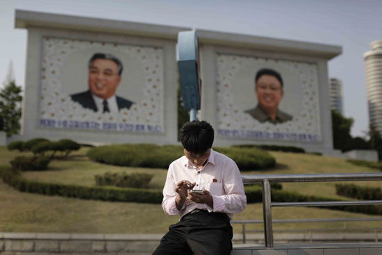 In this Tuesday, May 5, 2015, photo, a man sits in front of portraits of the late North Korean leaders Kim Il Sung, left, and Kim Jong Il, right, as he uses his smartphone in Pyongyang, North Korea. North Korean officials have unveiled a mobile-friendly online shopping site. (AP Photo/Wong Maye-E)