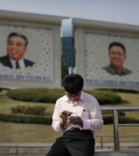 In this Tuesday, May 5, 2015, photo, a man sits in front of portraits of the late North Korean leaders Kim Il Sung, left, and Kim Jong Il, right, as he uses his smartphone in Pyongyang, North Korea. North Korean officials have unveiled a mobile-friendly online shopping site. (AP Photo/Wong Maye-E)