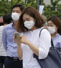 A woman wearing a mask as a precaution against the MERS, Middle East Respiratory Syndrome, virus uses her smartphone on the street in Seoul, South Korea, Tuesday, June 2, 2015. (AP Photo/Ahn Young-joon)