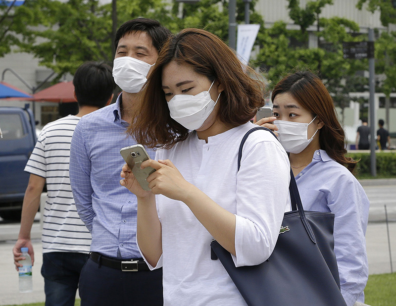 A woman wearing a mask as a precaution against the MERS, Middle East Respiratory Syndrome, virus uses her smartphone on the street in Seoul, South Korea, Tuesday, June 2, 2015. (AP Photo/Ahn Young-joon)