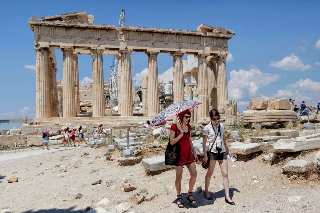 Tourists walk trough the ancient Acropolis hill, with the ruins of the fifth century BC Parthenon temple on the background in Athens, Monday, June 29, 2015. Anxious Greeks lined up at ATMs as they gradually began dispensing cash again on the first day of capital controls imposed in a dramatic twist in Greece's five-year financial saga. Banks will remain shut until next Monday, and a daily limit of 60 euros ($67) has been placed on cash withdrawals from ATMs. (AP Photo/Daniel Ochoa de Olza)