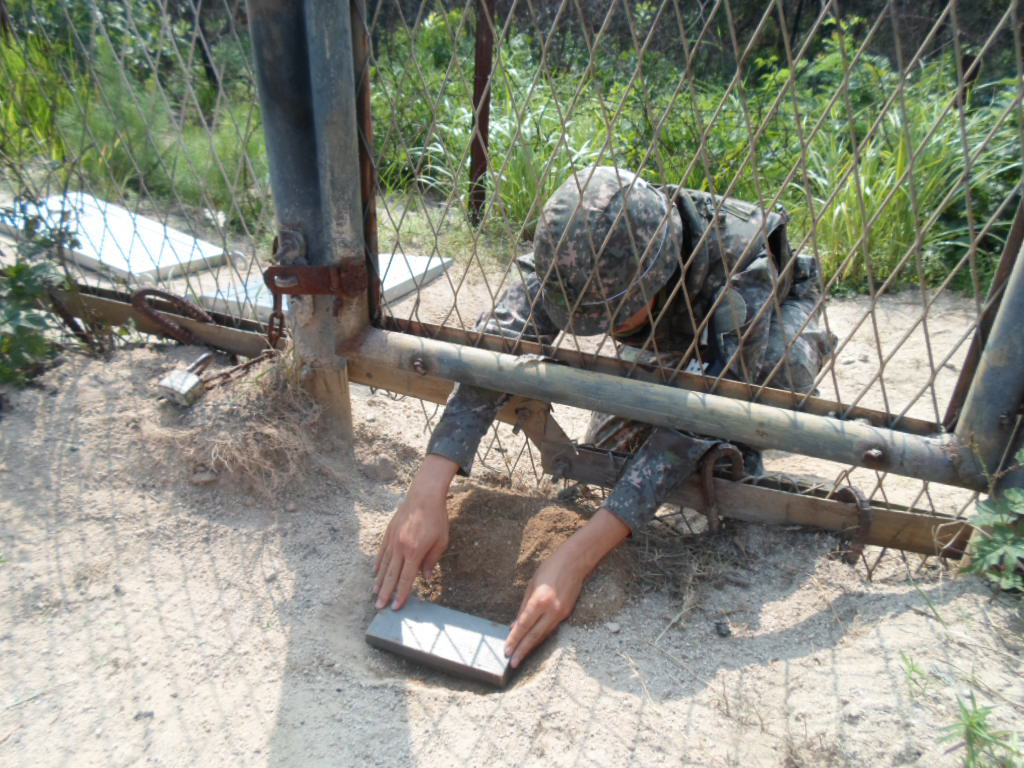 A South Korean soldier re-enacts planting of a wooden-box mine on the south side of the demilitarized zone (DMZ) fence near the city of Paju, on Aug. 9, 2015, in this photo released on Aug. 10, by the Joint Chiefs of Staff. North Korea is believed to have masterminded the Aug. 4 incident in which the explosion of wooden-box mines severed the legs of two South Korean staff sergeants on a regular scouting mission, the Defense Ministry said Aug. 10. (Yonhap)