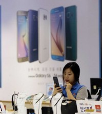 An employee of Samsung Electronics Co. watches a mobile phone near an advertisement of Samsung Electronics' Galaxy S6 and S6 Edge smartphone at a Samsung Electronics shop in Seoul, South Korea, Thursday, July 30, 2015. Samsung Electronics reported Thursday a fifth straight drop in quarterly earnings as the Galaxy S6 failed to reverse its declining fortunes in the smartphone industry. (AP Photo/Ahn Young-joon)