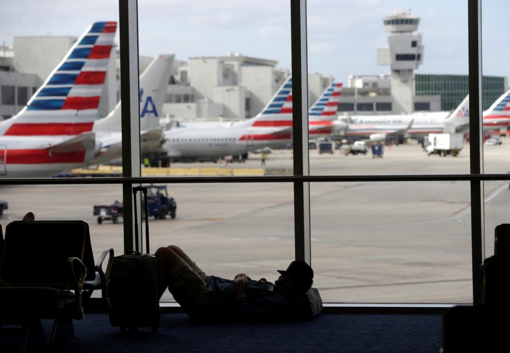 A traveler rests on the floor as American Airlines aircraft are lined up the the gates at Miami International Airport, Tuesday, Nov. 24, 2015, in Miami. Thanksgiving is one of the busiest travel holidays of the year, both in the air and on the roads. (AP Photo/Lynne Sladky)