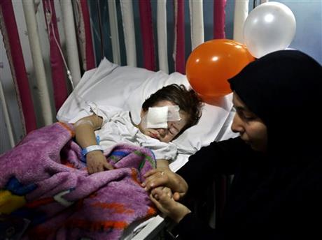 FILE - In this Friday, Nov. 13, 2015 file photo, Adraa Taleb holds the hand of her maternal cousin Haidar Mustafa, three, who was wounded in Thursday's twin suicide bombings, as he sleeps on a bed at the Rasoul Aazam Hospital in Burj al-Barajneh, southern Beirut, Lebanon. Haidar's parents Hussein and Leila were killed in the blast as they were parking their car when one of two suicide attackers blew himself up in a southern Beirut suburb near their vehicle. Within hours of the Paris attacks last week that left 129 dead, outrage and sympathy flooded social media feeds and filled the airwaves. Commenting on the public outpouring of support and anger following the Paris attacks, Lebanese blogger Joey Ayoub accused the media and world leaders of caring less about deaths in Beirut in IS attacks than deaths in Paris at the hands of the same group. (AP Photo/Bilal Hussein, File)