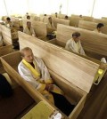 Wang Yong-yo, left bottom, sits inside a wooden coffin during the “death experience” program at Hyowon Healing Center in Seoul, South Korea, Tuesday, Dec. 22, 2015. In a dark, dimly-lit room, people dressed in white burial shrouds sit down next to dozens of coffins. They write their wills, climb into the caskets, lie down and a symbolic “angel of death” _ a man wearing a traditional Korean hat and black robes -- shuts the lid of each casket.(AP Photo/Ahn Young-joon)