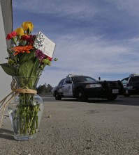 Flowers are left by the side of the road as a San Bernardino police officer blocks the road leading to the site of yesterday's mass shooting on Thursday, Dec. 3, 2015 in San Bernardino, Calif. A heavily armed man and woman dressed for battle opened fire on a holiday banquet for his co-workers Wednesday, killing multiple people and seriously wounding others in a precision assault, authorities said. Hours later, they died in a shootout with police. (AP Photo/Chris Carlson)