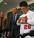 New St. Louis Cardinals relief pitcher Seung-Hwan Oh puts on his new jersey on Monday, Jan. 11, 2016, during a news conference as Cardinals manager Mike Matheny, left, and Senior Vice President and General Manager John Mozeliak look on, at Busch Stadium, in St. Louis. (J.B. Forbes/St. Louis Post-Dispatch via AP)