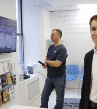 In this March 9, 2016, photo, Joe Silverman, right, poses in the lobby of his New York computer repair shop while employee Alex Lokshin watches the company's big-screen TV. Silverman realized last year he was losing productivity to the NCAA college basketball tournament, as the 20 staffers of his computer repair company kept checking their phones for scores during the games. His solution was to allow them to have the games on the big-screen TV he had installed for customers, but to let them know they do need to focus on their tasks at hand. Silverman keeps an eye on the games, too. (AP Photo/Mark Lennihan)