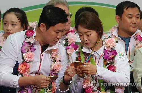 South Korean shooter Jin Jong-oh (L) touches archer Chang Hye-jin's Olympic gold medal during a ceremony to disband the South Korean delegation to the Rio de Janeiro Olympics at Incheon International Airport, west of Seoul, on Aug. 24, 2016.