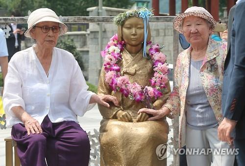 South Korean "comfort women" forced into brothels for the Japanese military during World War II -- Kim Bok-dong (L) and Kil Won-ok -- pose for a photo with the Peace Monument, a statue of a young girl that symbolizes the Korean victims of the enforced sexual slavery, during a ceremony to unveil it in the southwestern city of Jeonju on Aug. 13, 2015.