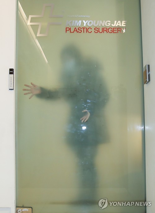 An employee at plastic surgeon Kim Young-jae's office in Seoul is visible through a glass door as independent counsel team investigators arrive for a search on Dec. 28, 2016. Kim's office was one of the cosmetic surgery clinics raided on that day as part of the ongoing probe into allegations related to President Park Geun-hye and her confidante Choi Soon-sil. Kim is believed to have provided treatment to the president with Choi's help without going through due security procedures.