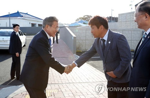 President Moon Jae-in (L) shakes hands with the head of Gangjeong, a small fishing town on the southern coast of Jeju Island, as he meets with local residents on Oct. 11, 2018. (Yonhap)