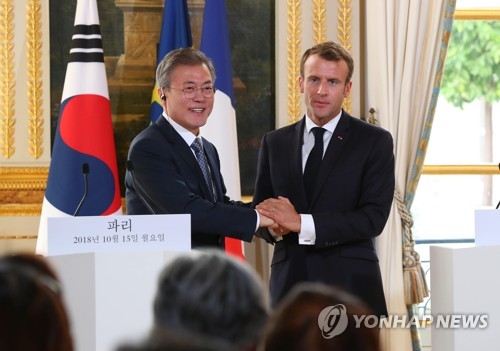 South Korean President Moon Jae-in (L) and French President Emmanuel Macron clasp hands after holding a joint press conference to announce the outcome of their bilateral summit at the Elysee Palace in Paris on Oct. 15, 2018. (Yonhap)